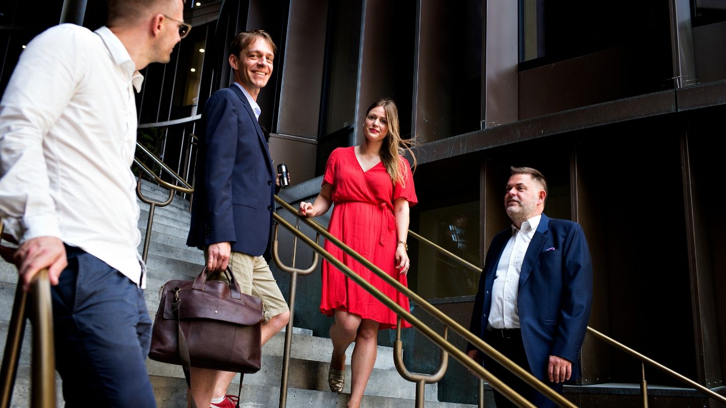 Kvinde i rød kjole og tre mænd i jakkesæt