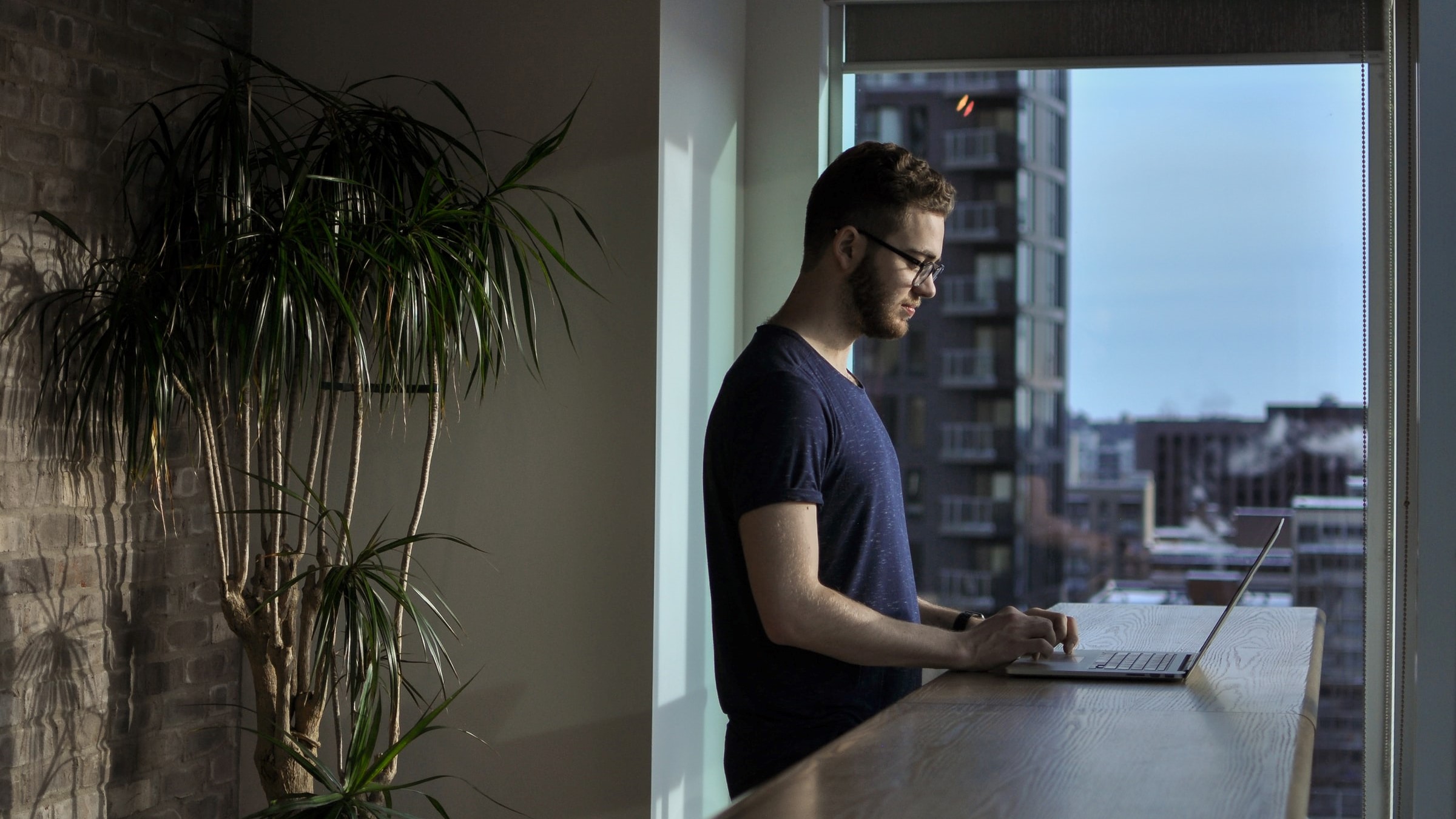 Man standing beside table using laptop